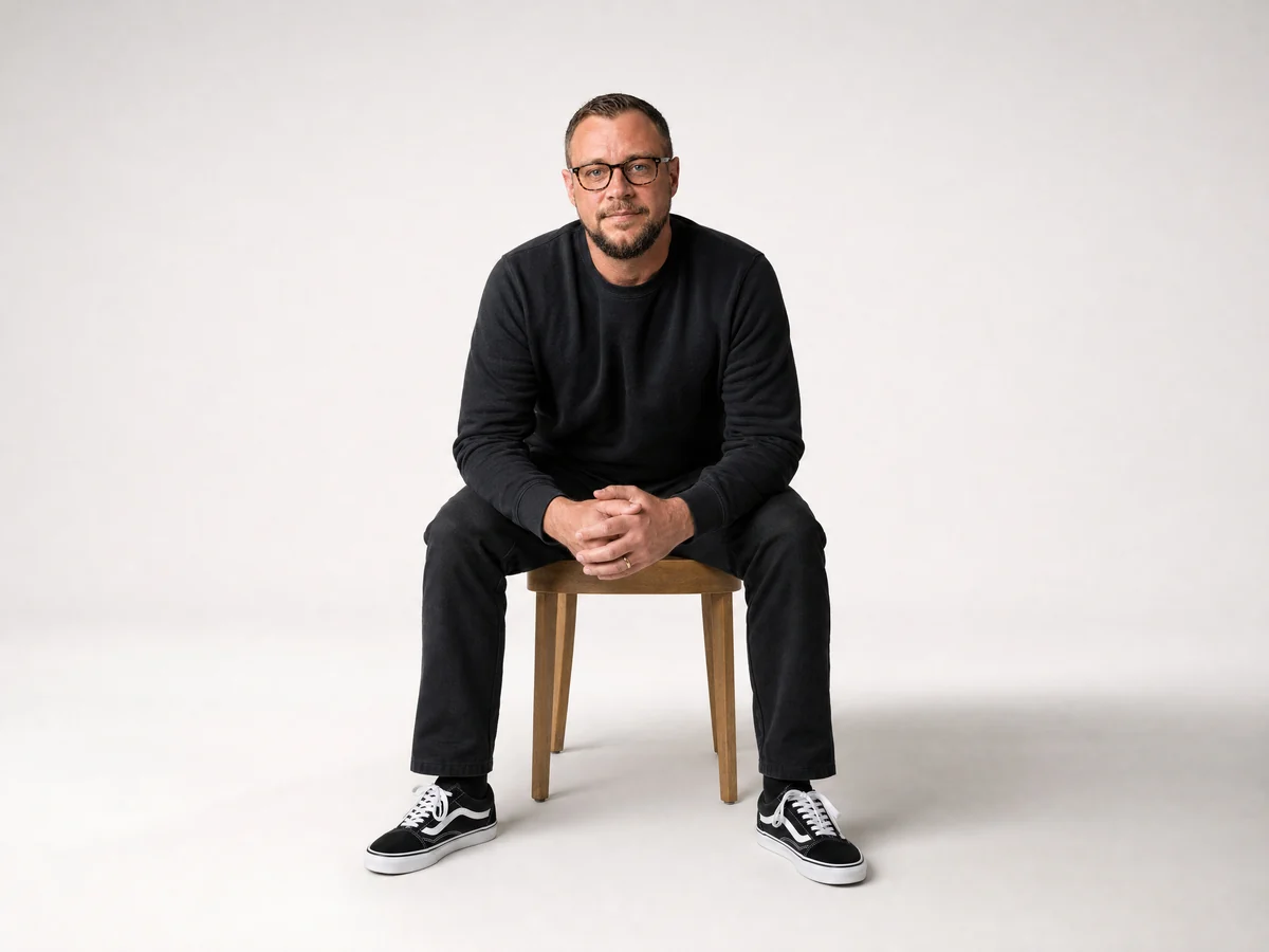 Valentin sitting forward on a wooden chair, wearing black and smiling at the camera
